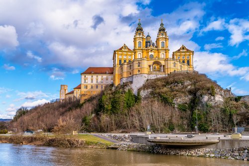 Herbstliche Ansicht der Abtei Melk in Österreich, umgeben von buntem Laub und der Donau im Vordergrund.