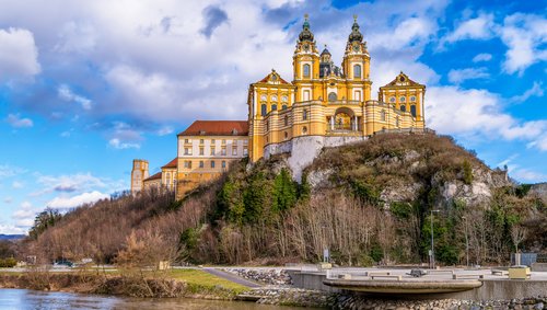 Herbstliche Ansicht der Abtei Melk in Österreich, umgeben von buntem Laub und der Donau im Vordergrund.