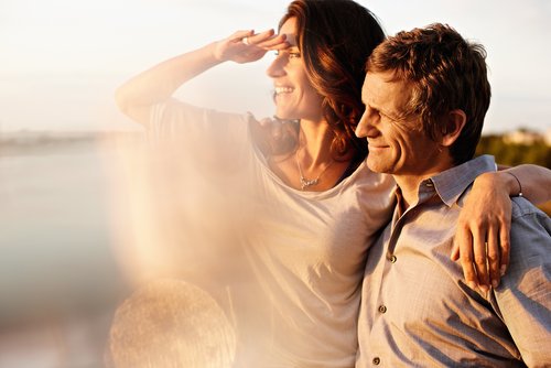 Ein Paar blickt vom Sonnendeck eines Flusskreuzfahrtschiffs auf den Rhein bei Sonnenschein. Die Frau hält sich die Hand an die Augenbrauen, um in die Ferne zu blicken.