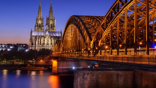 Kölner Dom und beleuchtete Hohenzollernbrücke über den Rhein bei Abenddämmerung in Köln