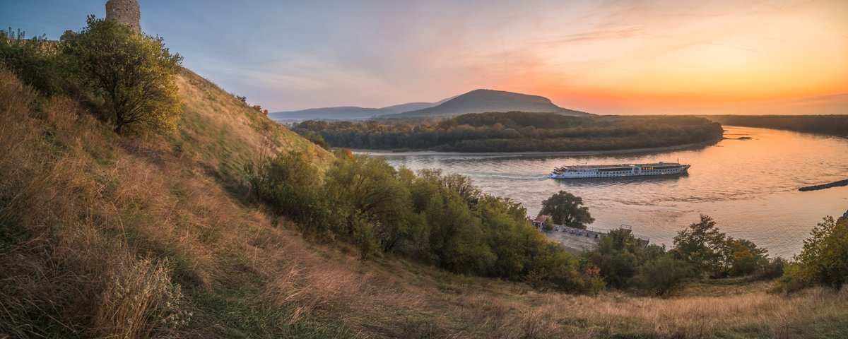 Panoramablick vom Ufer auf die Donau bei Bratislava während des Sonnenuntergangs. Ein Flussschiff fährt vorbei.