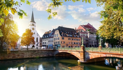 Straßburger Altstadt mit Fachwerkhäusern und Kanälen, umgeben von grünen Bäumen, unter blauem Himmel.