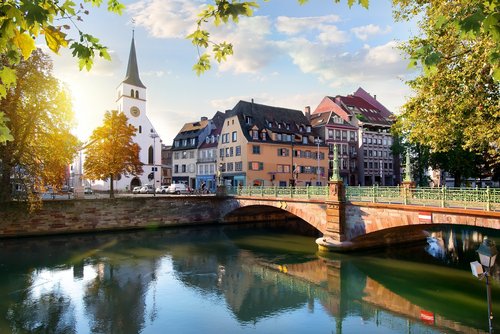 Straßburger Altstadt mit Fachwerkhäusern und Kanälen, umgeben von grünen Bäumen, unter blauem Himmel.