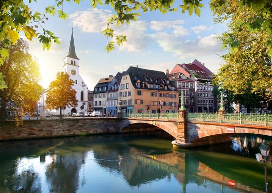Straßburger Altstadt mit Fachwerkhäusern und Kanälen, umgeben von grünen Bäumen, unter blauem Himmel.