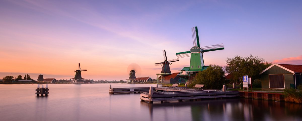 Traditionelle niederländische Windmühlen und Holzhäuser am Wasser in Zaanse Schans während des Sonnenuntergangs