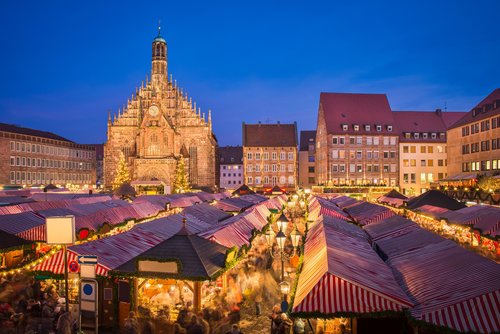 Weihnachtsmarkt in Nürnberg bei Abenddämmerung mit beleuchteten Ständen und der beleuchteten Frauenkirche im Hintergrund