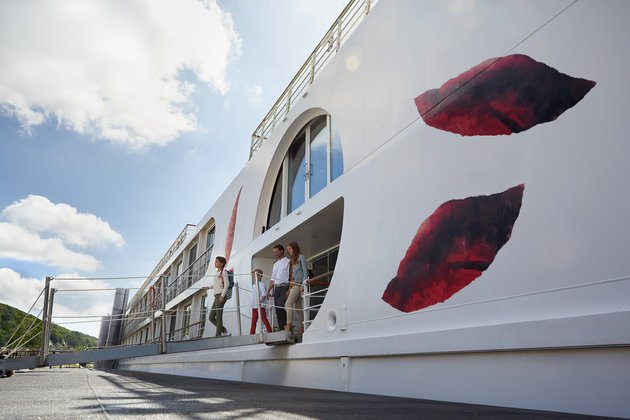 Familie mit zwei Kindern steigt über eine Gangway von einem weißen Flusskreuzfahrtschiff auf einen Landungssteg aus.