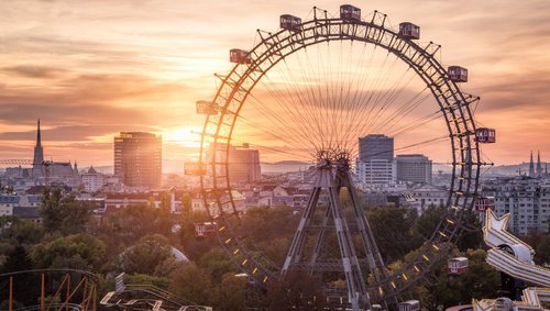 Blick auf die Wiener Innenstadt mit dem Wiener Parter und einem großen Riesenrad im Vordergrund, bei Sonnenuntergang.