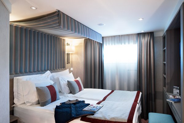 Eine stilvoll eingerichtete Kabine auf der A-ROSA ALVA mit Doppelbett, Schreibtisch und Fenster bei Tageslicht.