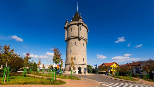 Blick auf den Wasserturm in der Stadt Turnu Severin, um den eine Straße führt. Im Vordergrund ist eine Kreuzung und ein Fußweg mit kleinen Bäumen zu sehen.