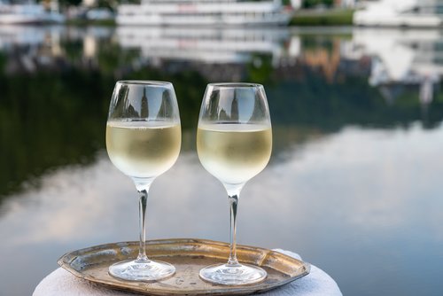 Zwei Weingläser mit Weißwein auf einem Tablett, im Hintergrund ein Fluss