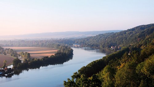 Fluss Seine fließt durch bewaldete Hügel und Felder bei klarem Himmel in der Normandie. 