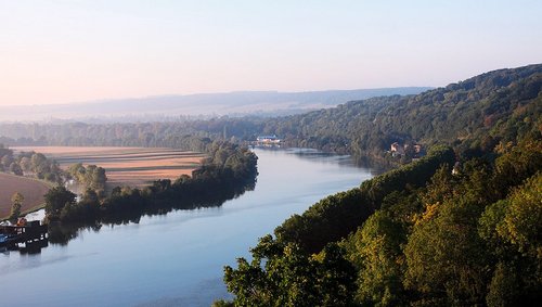 Fluss Seine fließt durch bewaldete Hügel und Felder bei klarem Himmel in der Normandie. 