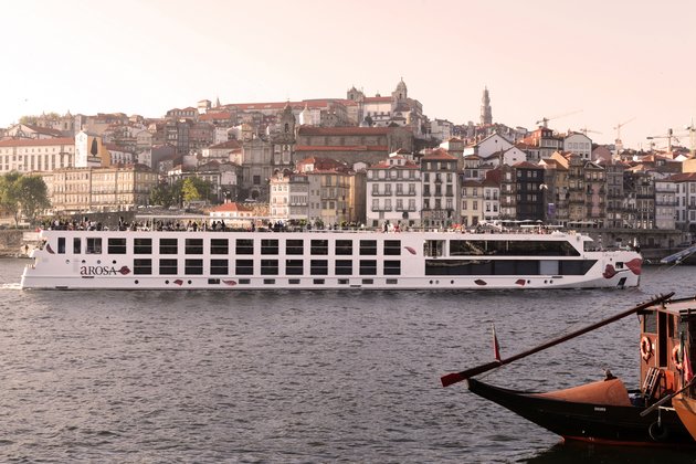 Flusskreuzfahrtschiff A-ROSA ALVA auf dem Douro vor einer Stadt mit historischen Gebäuden und roten Dächern.