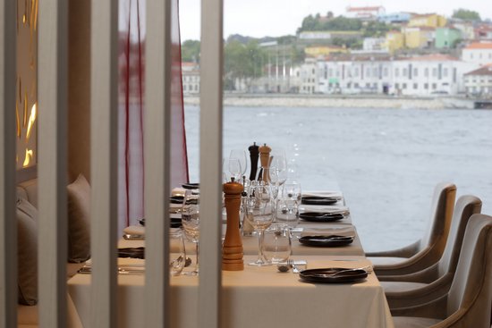 Eleganter Esstisch im Restaurant des Flusskreuzfahrtschiffs A-ROSA ALVA mit gedeckten Plätzen und Blick auf das Wasser und eine Stadt am Ufer.
