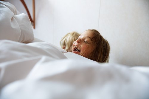 Zwei Kinder spielen neben dem Bett in einer Kabine auf einem Flusskreuzfahrtschiff. Ein Kind schaut lachend über den Rand des Bettes.