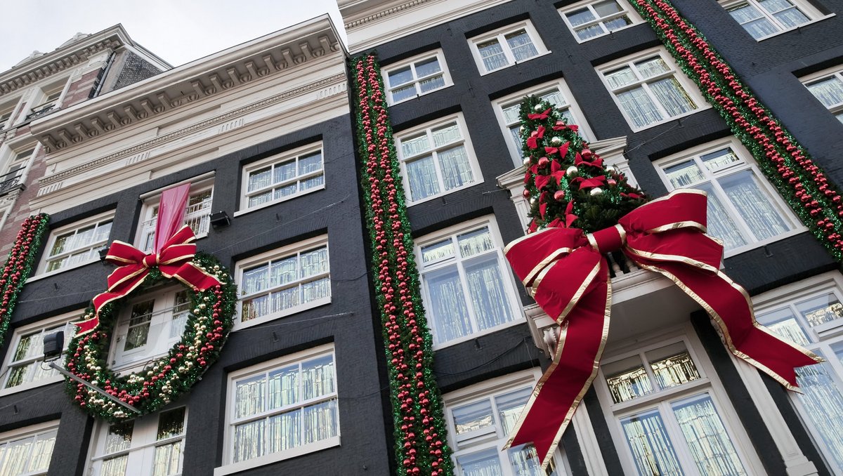 Weihnachtlich geschmückte Häsuer in Amsterdam. Große Schleifen und Weihnachtskugeln sowie ein Weihnachtsbaum sind an den Hausfassaden angebracht.