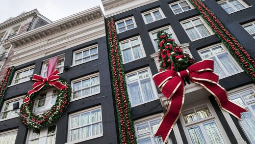 Weihnachtlich geschmückte Häsuer in Amsterdam. Große Schleifen und Weihnachtskugeln sowie ein Weihnachtsbaum sind an den Hausfassaden angebracht.