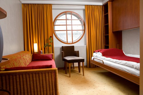 Eine Kabine der Kategorie S an Bord der A-ROSA LUNA und A-ROSA STELLA. Einrichtet in warmen Farben mit zwei Einzelbetten und Bullaugen als Fenstern. An der Wand ist ein Pullmanbett, dass man runterklappen kann.