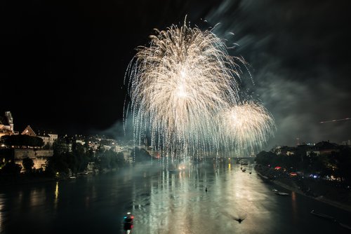Feuerwerk erleuchtet den Nachthimmel über Basel, reflektiert im Rhein