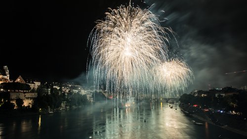 Feuerwerk erleuchtet den Nachthimmel über Basel, reflektiert im Rhein