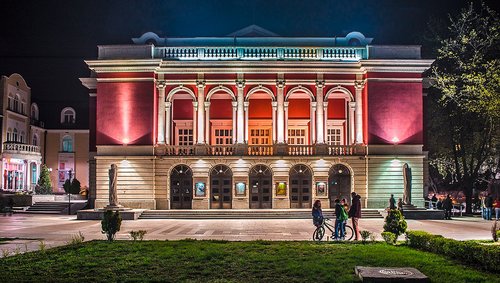 Blick auf das Opernhaus Rousse, beleuchtet bei Nacht mit Personen davor.