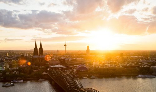 Panoramablick auf die Stadt Köln mit dem Kölner Dom bei Sonnenuntergang. Im Vordergrund die Hohenzollernbrücke, die über den Rhein führt.