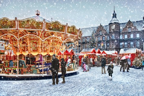 Verschneiter Weihnachtsmarkt in Düsseldorf mit Spaziergängern und einem Karussell im Vordergund und Ständen im Hintergrund