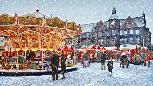 Verschneiter Weihnachtsmarkt in Düsseldorf mit Spaziergängern und einem Karussell im Vordergund und Ständen im Hintergrund
