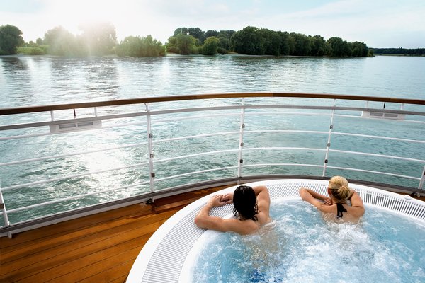 Zwei Personen entspannen am Nachmittag im Whirlpool an Deck mit Blick auf den ruhigen Fluss und grüne Uferlandschaft.