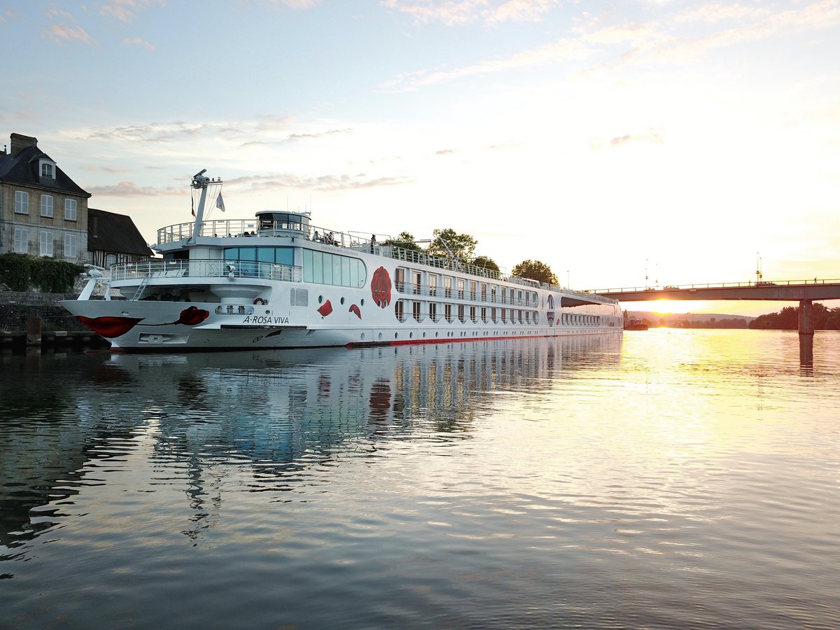 Flusskreuzfahrtschiff A-ROSA VIVA am Ufer bei Sonnenuntergang mit Brücke im Hintergrund.