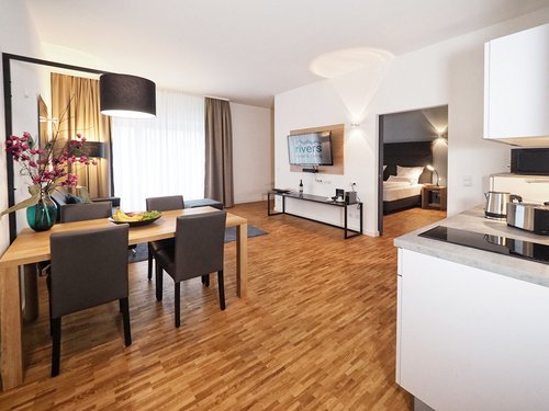 Ein modernes Appartement im Appartementhotel Rivers in Passau an der Donau mit Schlafzimmer, Küche und Essbereich sowie Wohnbereich mit Flachbildfernseher.