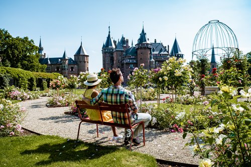 Zwei Personen sitzen auf einer Bank in einem blühenden Rosengarten mit Blick auf ein historisches Schloss in Utrecht