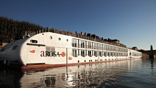 Die A-ROSA STELLA liegt am Ufer in einer Stadt an der Rhône bei Sonnenaufgang, im Hintergrund eine Brücke und Gebäude. 