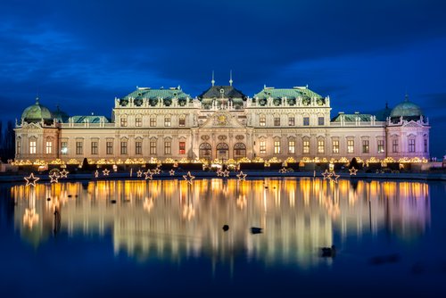 Beleuchtetes Schloss Belvedere in Wien bei Nacht mit Sternenlichtern und Spiegelung im Wasser