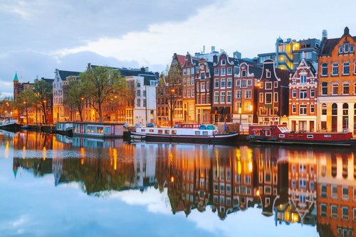 Blick auf Amsterdams Grachten mit historischen Gebäuden und Booten auf dem Wasser, während der Abenddämmerung.