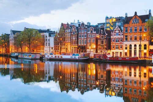 Blick auf Amsterdams Grachten mit historischen Gebäuden und Booten auf dem Wasser, während der Abenddämmerung.