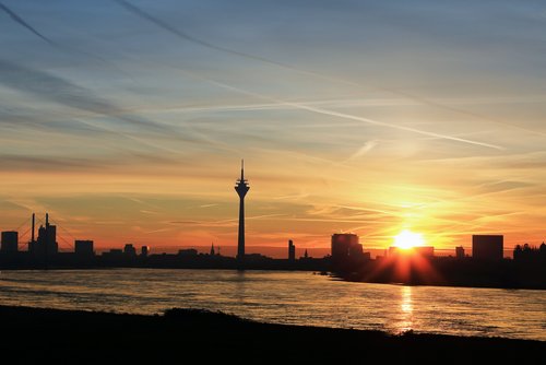 Blick auf die Düsseldorfer Skyline bei Sonnenuntergang, mit dem Rheinturm und modernen Gebäuden am Flussufer.