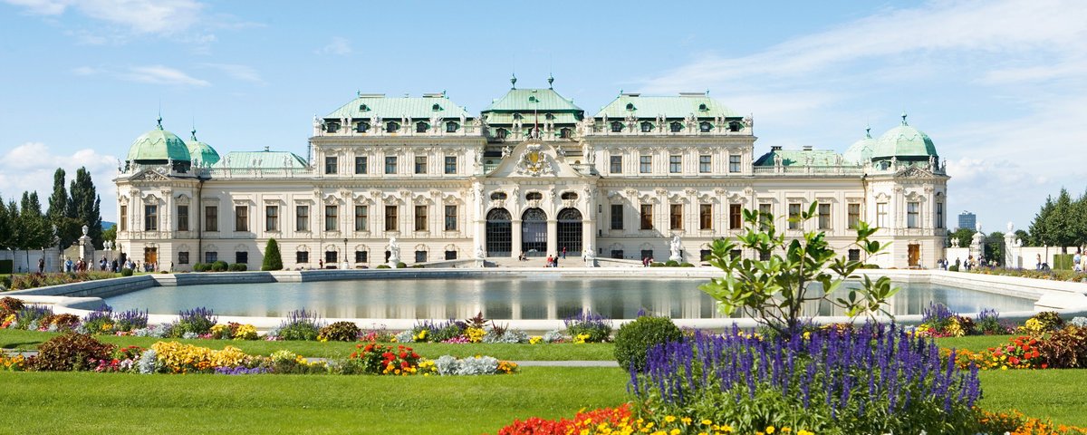 Das Schloss Belvedere in Wien, umgeben von gepflegten Gärten mit bunten Blumen und einem Brunnen bei sonnigem Wetter, mit barocker Architektur und kunstvollen Details.