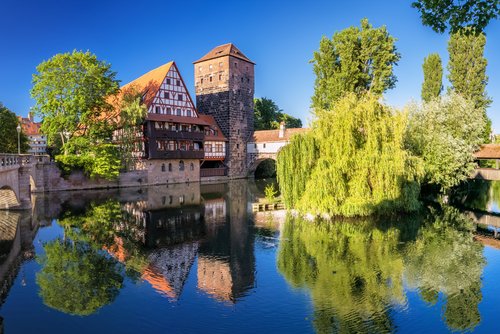 Blick auf die historische Altstadt von Nürnberg mit der Kaiserburg im Hintergrund, umgeben von grünen Bäumen und blauen Himmel.