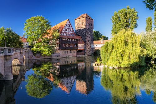 Blick auf die historische Altstadt von Nürnberg mit der Kaiserburg im Hintergrund, umgeben von grünen Bäumen und blauen Himmel.
