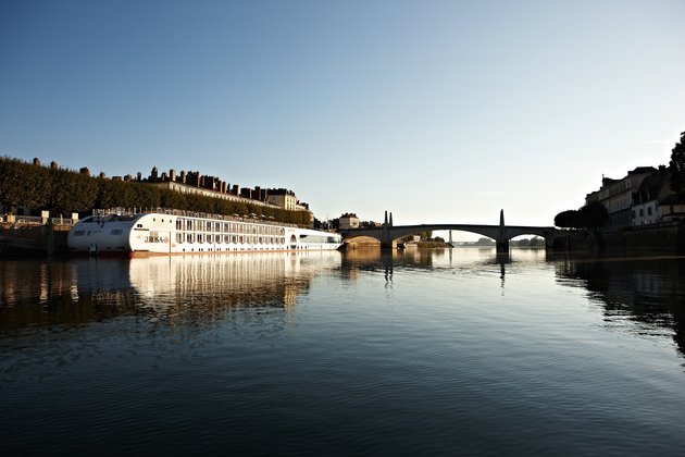 Die A-ROSA STELLA liegt am Ufer in einer Stadt an der Rhône bei Sonnenaufgang, im Hintergrund eine Brücke und Gebäude. 