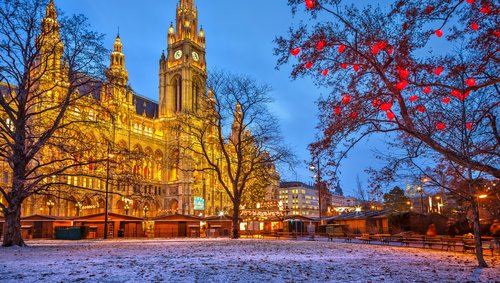 Beleuchtetes Wiener Rathaus bei Dämmerung mit winterlichem Park und roten Lichtern an Bäumen
