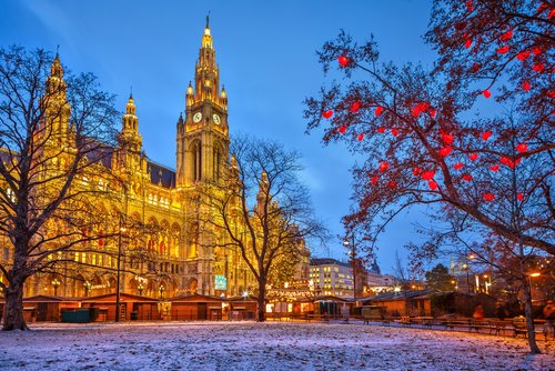 Beleuchtetes Wiener Rathaus bei Dämmerung mit winterlichem Park und roten Lichtern an Bäumen