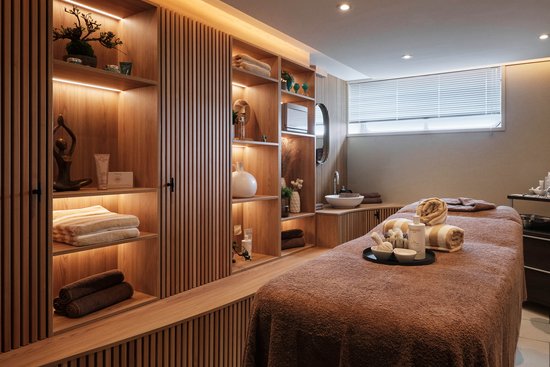 Stilvoller Behandlungsraum mit warmem Licht, Regalen mit Deko und Pflegeprodukten sowie einer Behandlungsliege.