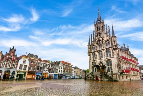 Historisches Rathaus mit gotischer Architektur und spitzen Türmen auf dem Marktplatz von Gouda, umgeben von traditionellen Gebäuden unter blauem Himmel