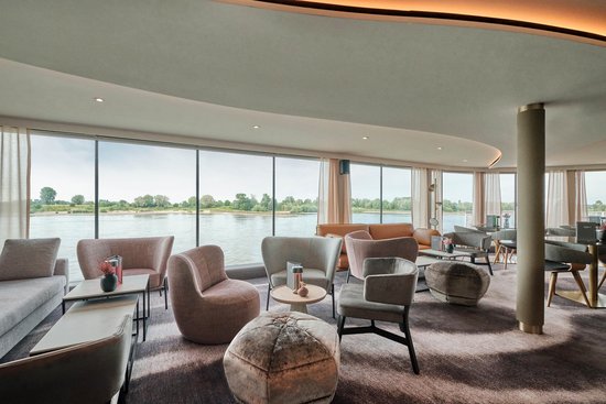 Moderne Lounge an Bord der A-ROSA SENA mit gemütlichen Sitzgelegenheiten, stilvoller Beleuchtung und bodentiefen Fenstern mit Blick auf den Fluss.