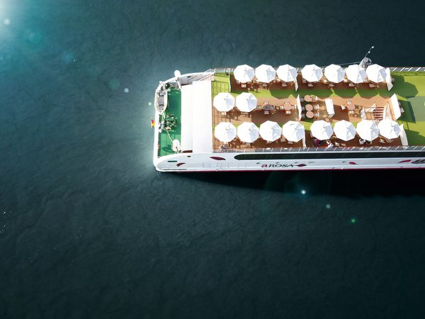 Draufsicht auf das Sonnendeck des Flusskreuzfahrtschiffs A-ROSA mit weißen Sonnenschirmen und Tischen auf dem Wasser.