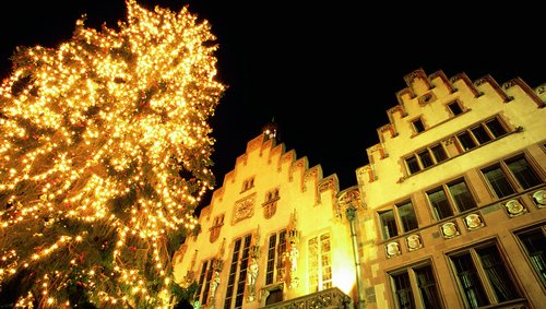 Weihnachtsbaum mit vielen Lichtern neben beleuchtetem historischem Gebäude am Römerberg in Frankfurt bei Nacht.