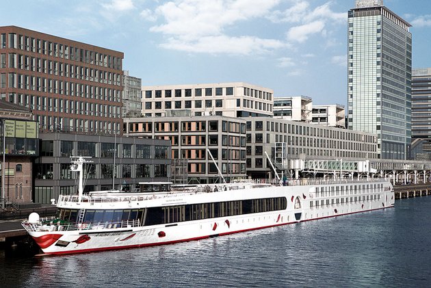 Die A-ROSA SILVA liegt tagsüber in einem Hafen vor modernen Bürogebäuden und Hochhäusern in städtischer Umgebung.